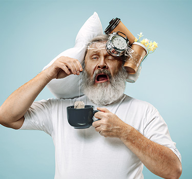 Overworked and tired old man yawns with items taped to his head and teacup in hand