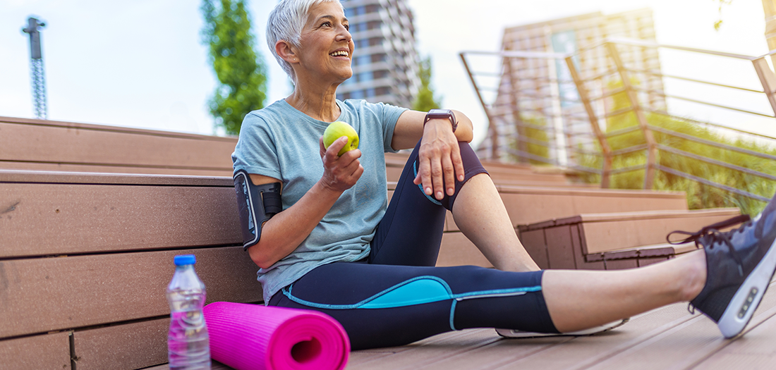 A senior woman sitting down after exercise eating an apple