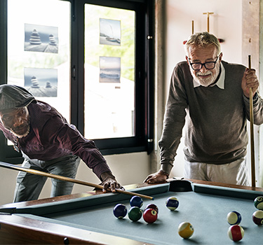 Three elder men playing a game of billiards in a clubhouse recreational room