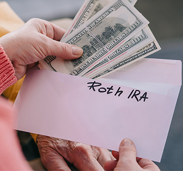 Woman opening an envelope, marked as Roth IRA, with hundred dollar bills inside