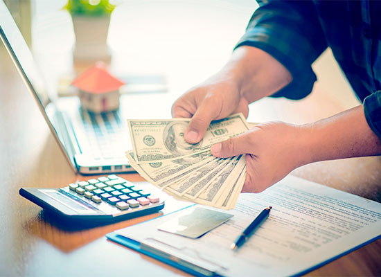 someone holding cash at a table with a laptop and calculator