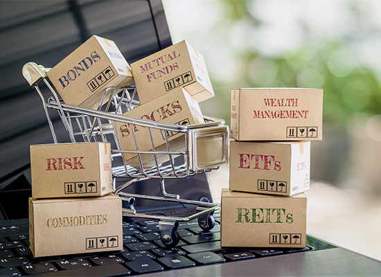 miniature shopping cart on a lapto keyboard, filled with labels such as mutual funds, bonds and stocks