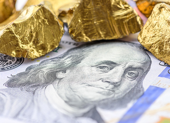 A close-up of gold nuggets on top of a U.S. hundred dollar bill, emphasizing the tangible value of gold as an investment.