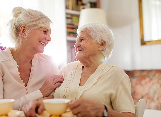 A elderly woman having tea and looking appreciatively at her daughter's care.