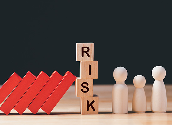 Wooden blocks spelling 'RISK' and dominoes in the background represent the potential risks in accumulation and decumulation phases of retirement savings and withdrawal strategies.