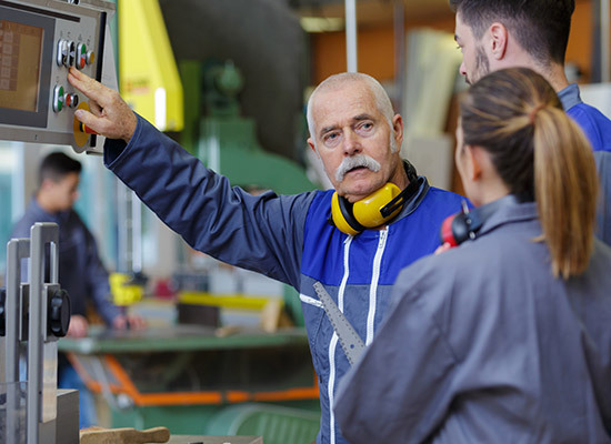 an older male teaching two younger adults in a factory