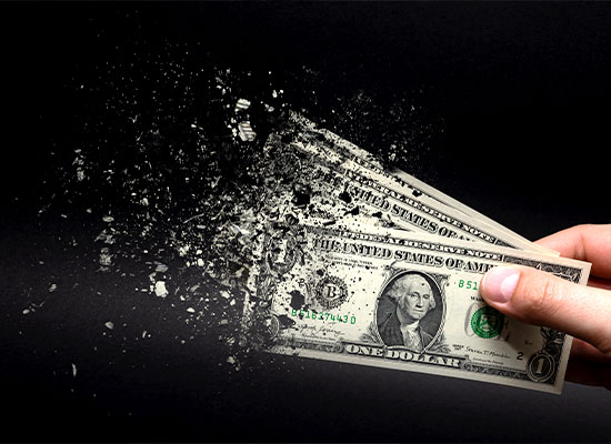 A hand holding a disintegrating one dollar bill against a dark background, implying the concept of money loss or devaluation.