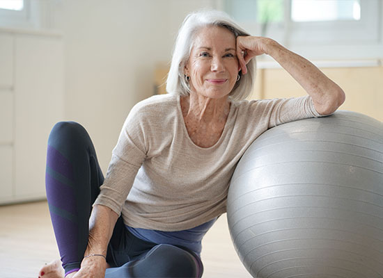 an older woman leaning against an exercise ball and posing for the camera