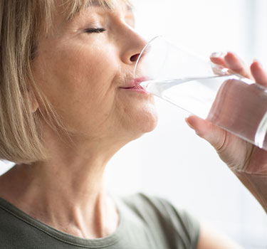 a senior woman drinking water out of a glass in order to stay healthy and hydrated
