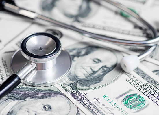 A stethoscope lies on a pile of us dollar bills, symbolizing the intersection of healthcare and finance