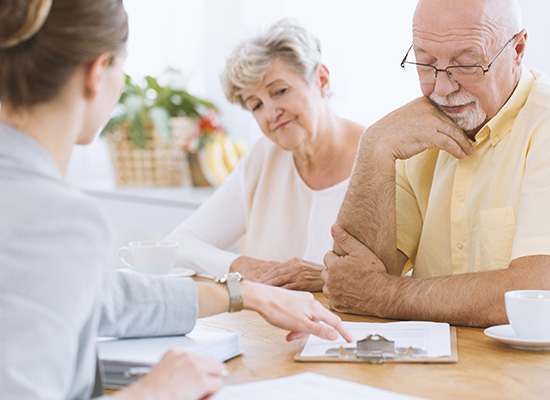 An elderly couple consults with a financial advisor, reviewing documents at a table, indicating a discussion on important financial planning.