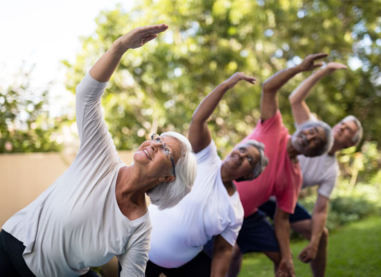 Group of retirees performing outdoor stretching exercises in an active retirement community, highlighting the cognitive and physical benefits of social activity, fall prevention, and adherence to senior exercise guidelines.