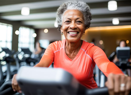 Older woman exercising on a stationary bike indoors, representing senior exercise guidelines and the importance of a retirement fitness plan for boosting health span and preventing falls.