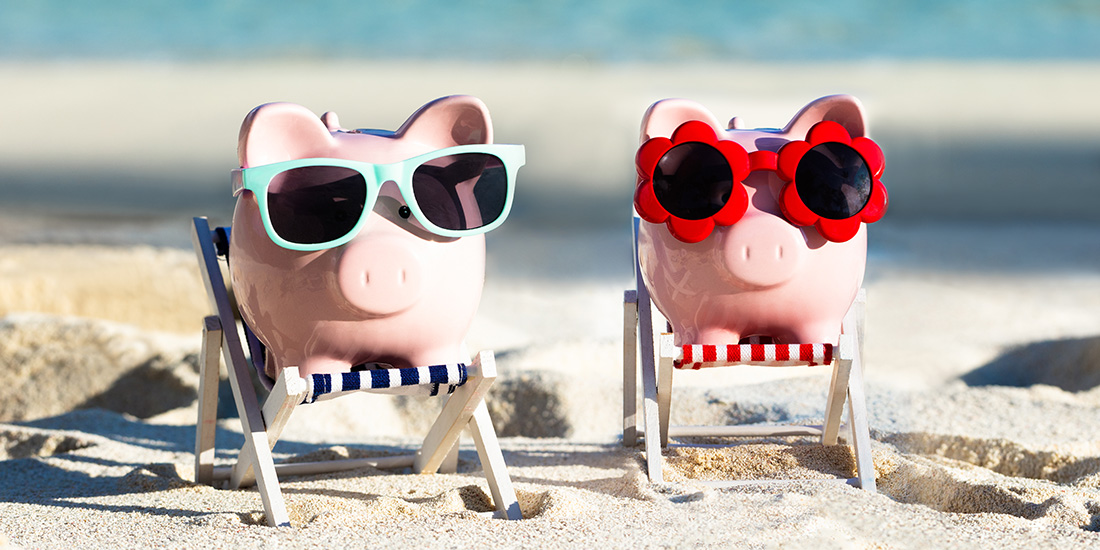 Two piggy banks on the beach wearing sunglasses