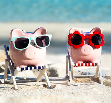 Two piggy banks on the beach wearing sunglasses