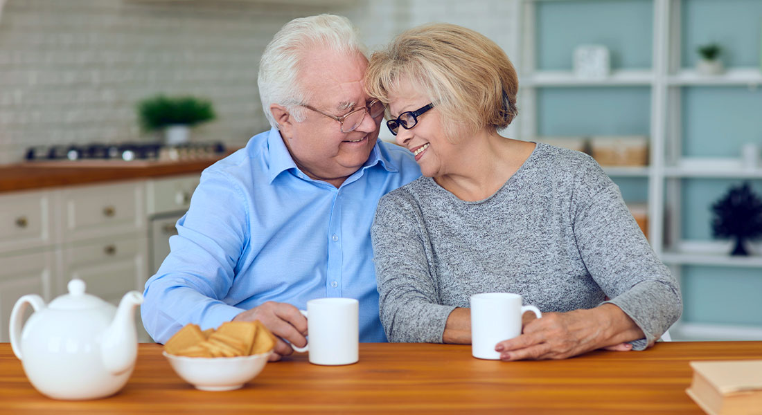 A happy older couple hugging and smiling together holding coffee cups