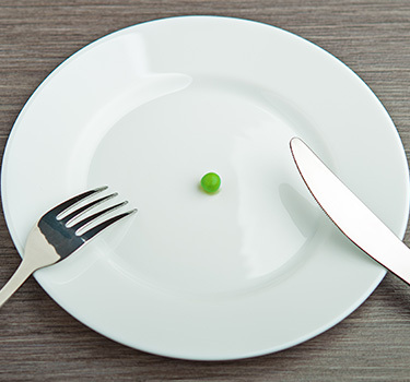 a plate with a single green pea, fork and knife on it