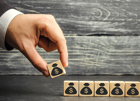 A hand places a wooden block with a money bag icon next to several others, symbolizing retirement income planning.