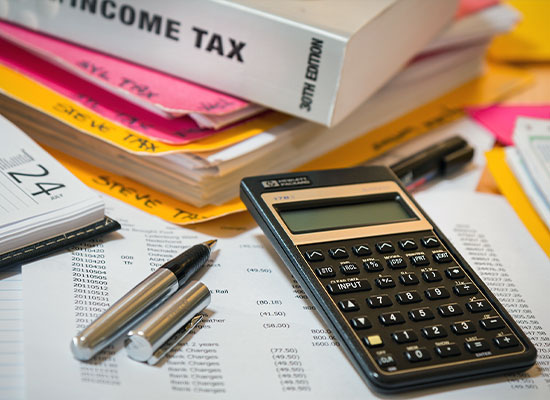 A calculator, pen, and highlighter rest on financial documents and spreadsheets with columns of numbers. 