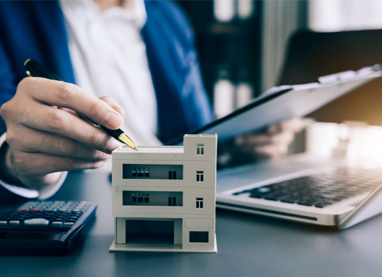 a business person holding documents at a computer with a model building on the desk