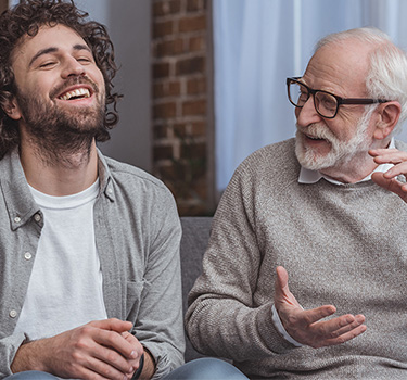 Old man laughing with young man on couch