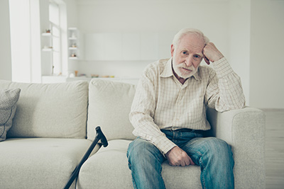 Lonely old man sitting alone at home with his cane