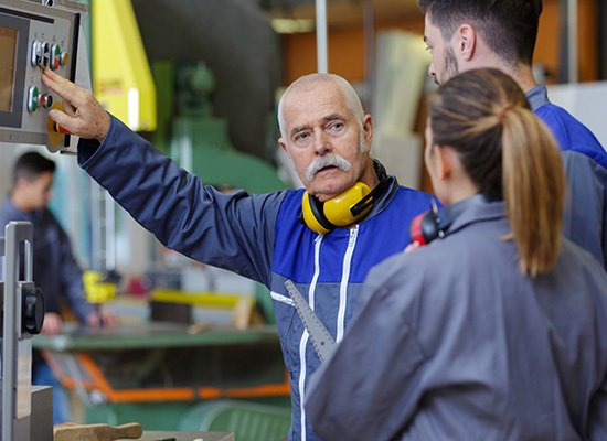 older man working in factory demonstrating controls to younger adults