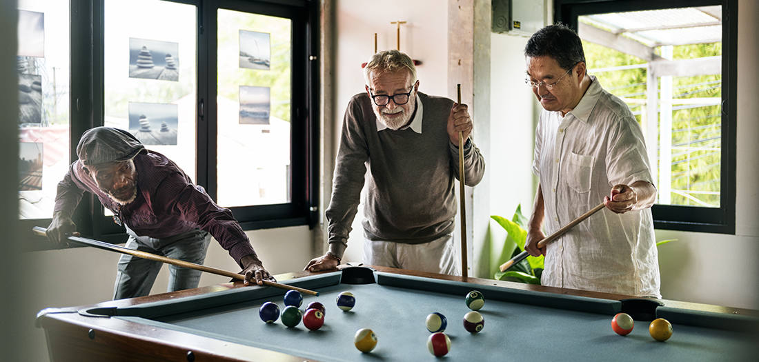 Three elder men playing a game of billiards in a clubhouse recreational room