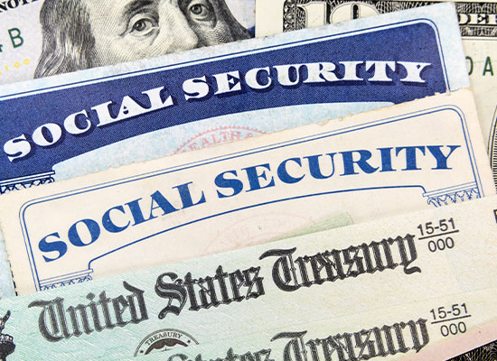 A social security check ontop of a social security card and cash.