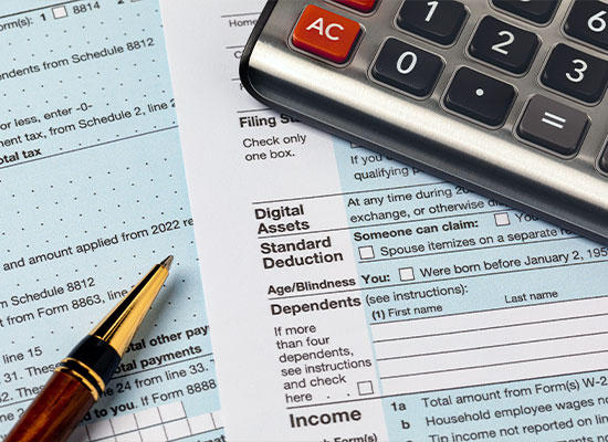 A close-up image of tax forms, a calculator, and a fountain pen on a desk, indicating preparation for filing taxes on digital assets.