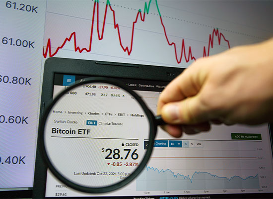 A person analyzes a computer screen displaying Bitcoin ETF trading data, magnifying a section showing bitcoin's price at 28.76 USD, down 2.87%, with a graphical background of fluctuating.